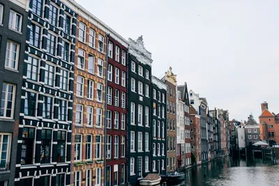 Обои на рабочий стол Вечерний Амстердам / Amsterdam в огнях, отраженных в  реке среди домов и дорог, Нидерланды / Netherlands, обои для рабочего  стола, скачать обои, обои бесплатно