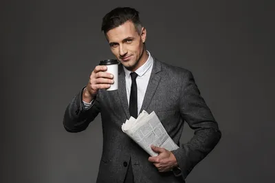 Фотография красивого делового мужчины, одетого в деловой костюм, пьющего  кофе на вынос в офисе и читающего газету, изолированного над серой стеной |  Премиум Фото