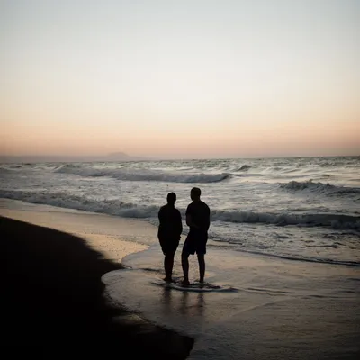 Пара гуляет на берегу моря в белых топах во время заката · Бесплатные  стоковые фото