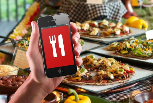 Еды Картинки рука, держащая красно-белый телефон перед столом с едой