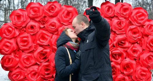 День Святого Валентина Картинки мужчина и женщина целуются перед большим букетом розовых цветов
