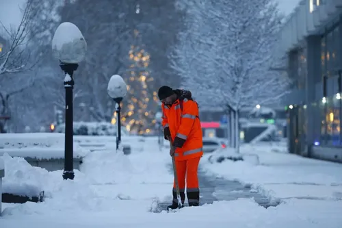 человек в оранжевой куртке убирает снег